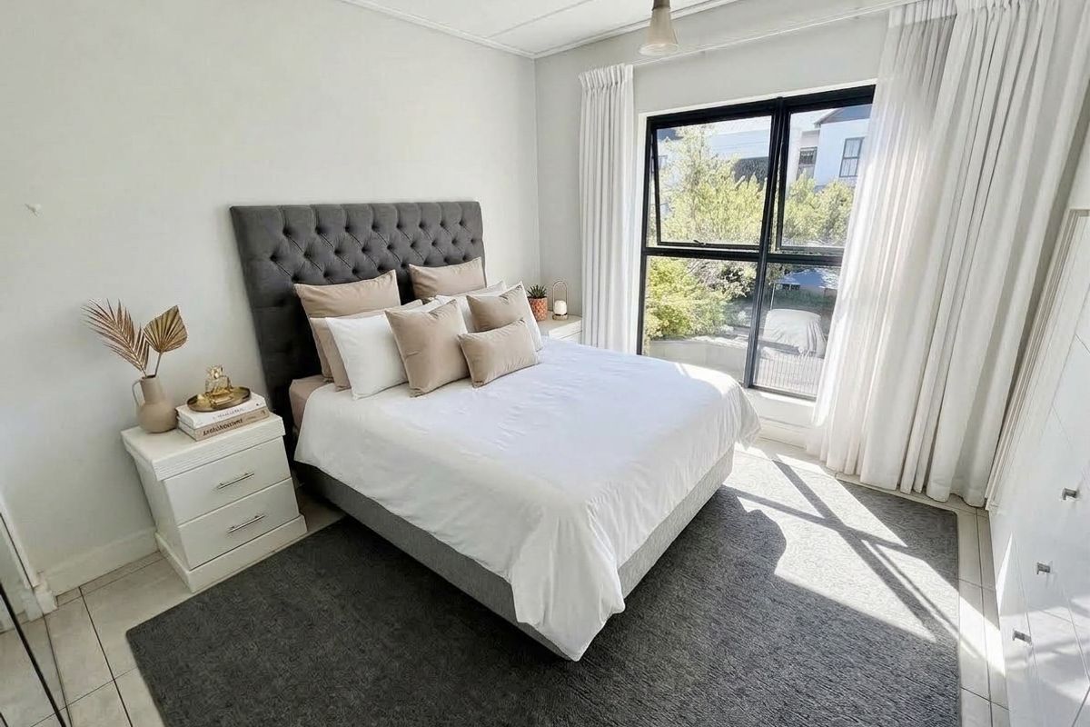 A bright and well-maintained bedroom featuring tiled flooring, a large black-framed window with natural light, and built-in wardrobe storage.