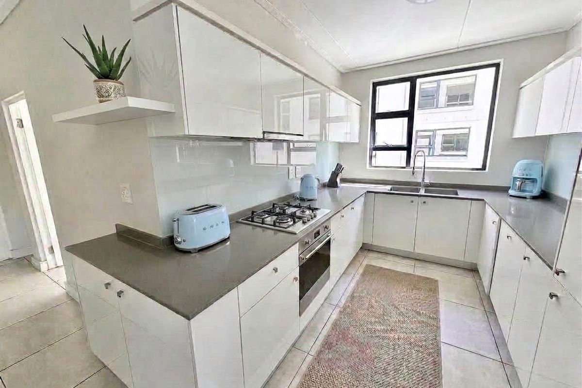 Modern kitchen featuring white high-gloss cabinetry, stone countertops, a gas hob, built-in oven, and a glass splashback with tiled flooring.