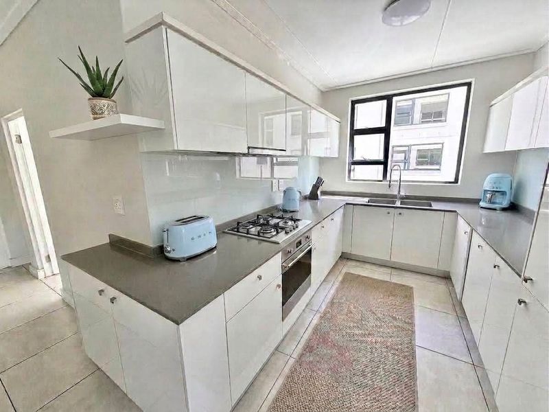 Modern kitchen featuring white high-gloss cabinetry, stone countertops, a gas hob, built-in oven, and a glass splashback with tiled flooring.