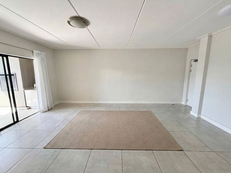 A bright, open-plan living area featuring neutral tiled flooring and a large sliding glass door providing access to an outdoor space.