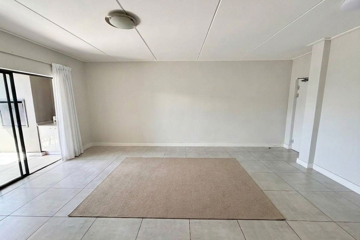 A bright, open-plan living area featuring neutral tiled flooring and a large sliding glass door providing access to an outdoor space.