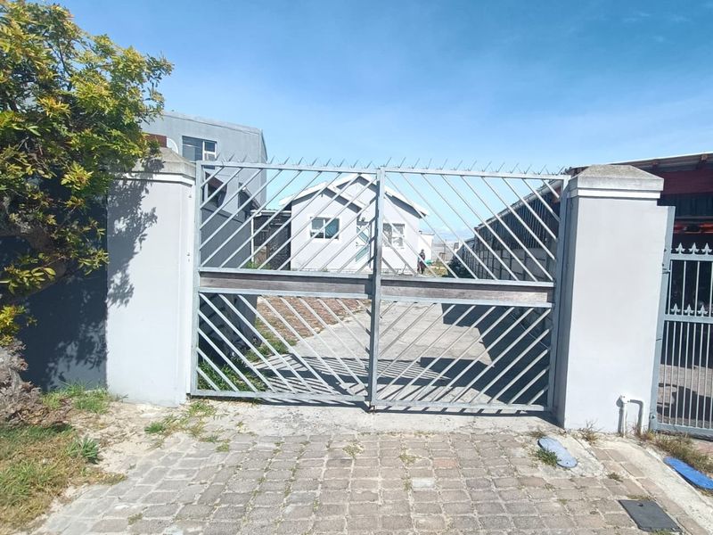Front view of the property featuring a secure metal gate, concrete pillars, and a paved driveway leading to the main house.