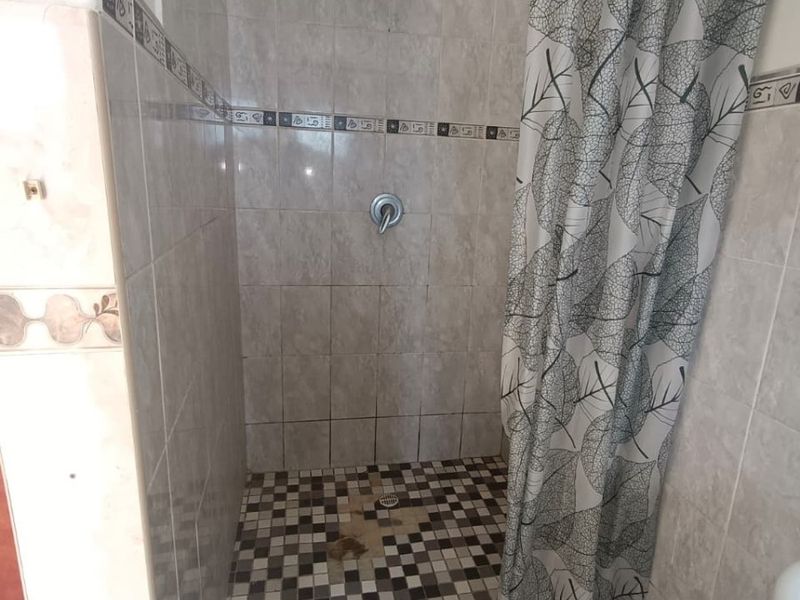 A shower enclosure featuring tiled walls and a mosaic-tiled floor with a fixed shower head and mixer.