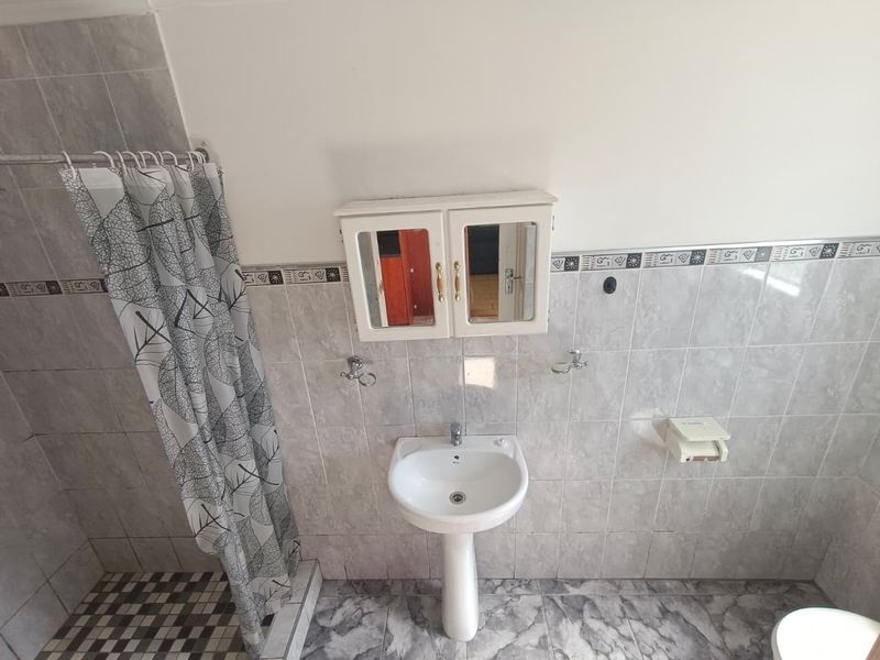 A functional bathroom featuring a pedestal basin, wall-mounted medicine cabinet, and tiled finishes throughout, providing a clean and practical space.