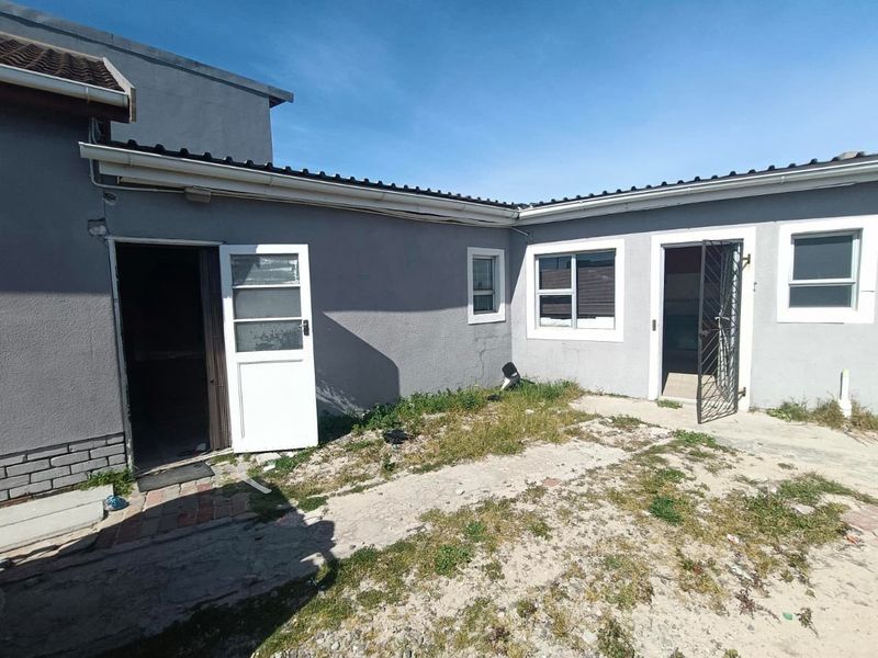 Rear exterior view of the property featuring plastered walls, tiled roofing, and access points with security gates, requiring landscaping and exterior maintenance.