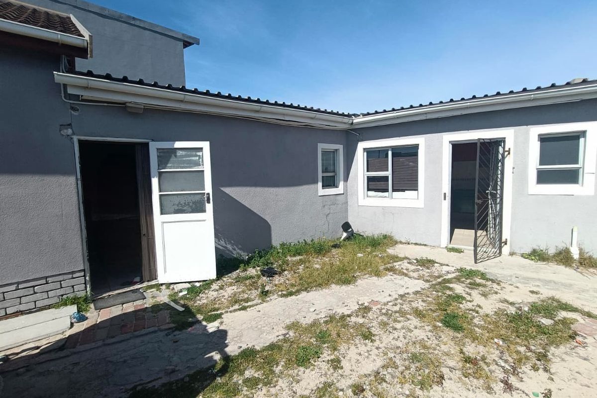 Rear exterior view of the property featuring plastered walls, tiled roofing, and access points with security gates, requiring landscaping and exterior maintenance.