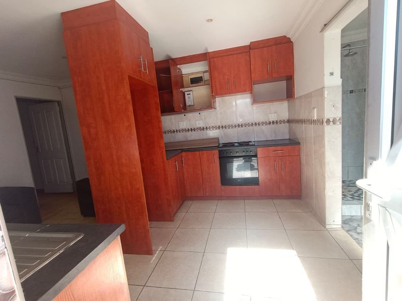 A functional kitchen featuring wood-finish cabinetry, built-in oven and hob, tiled flooring, and a tiled backsplash, offering a clean and practical workspace.