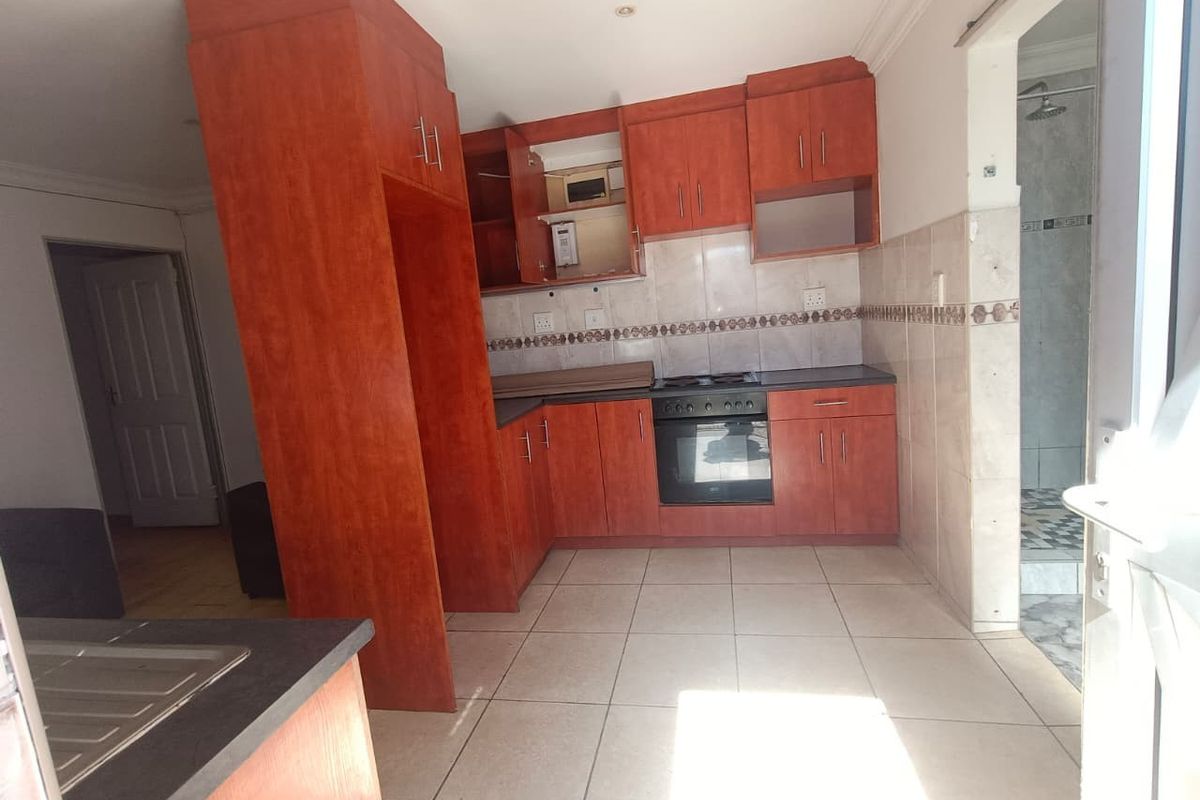 A functional kitchen featuring wood-finish cabinetry, built-in oven and hob, tiled flooring, and a tiled backsplash, offering a clean and practical workspace.