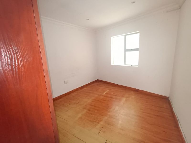 An empty bedroom featuring laminate flooring, built-in cupboards, and recessed downlights, offering a blank canvas for personalization.