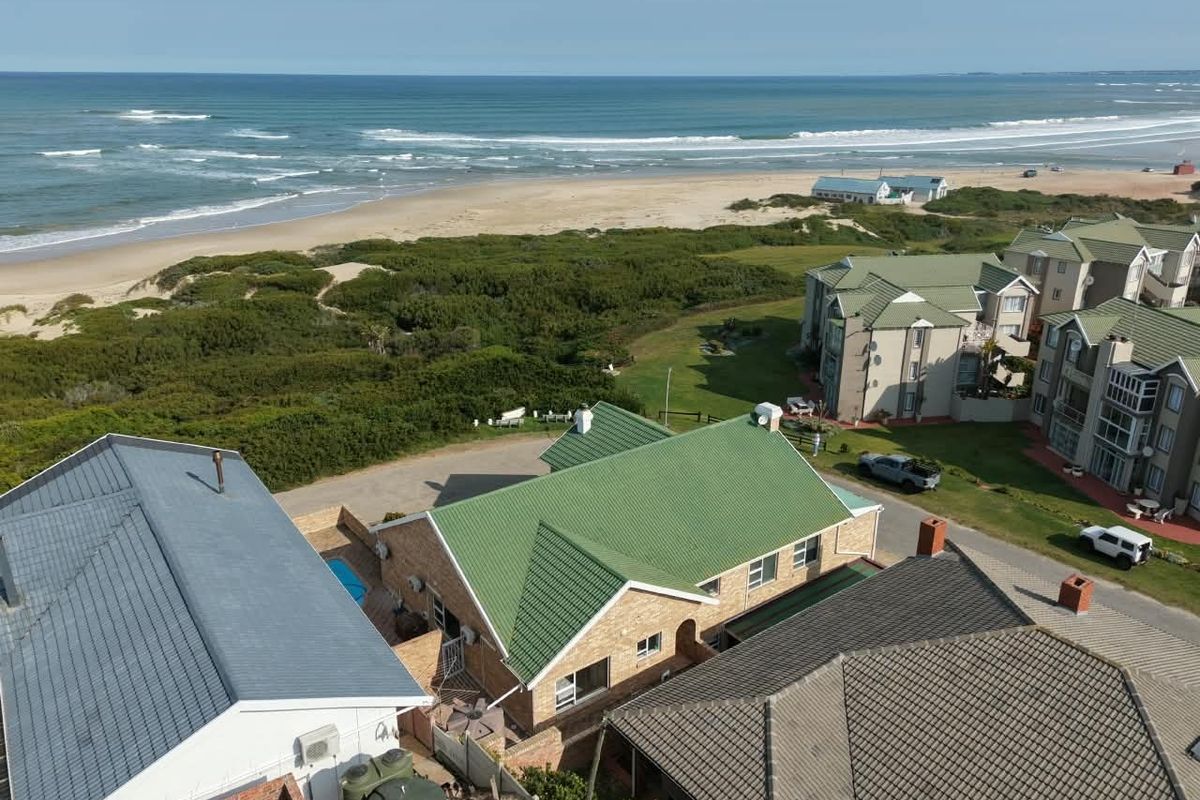 Aerial view of the property showcasing its proximity to the coastline, featuring a pitched roof, brick exterior, and surrounding residential context.