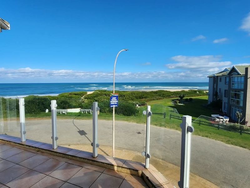 A spacious balcony featuring a modern glass balustrade and tiled flooring, offering expansive views of the coastline and surrounding landscape.