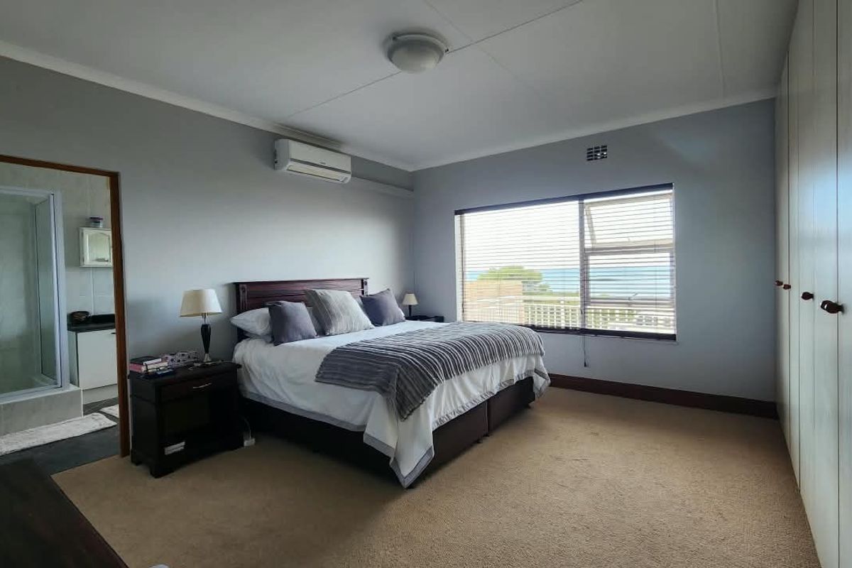 Spacious bedroom featuring built-in cupboards, carpeted flooring, an air conditioning unit, and an en-suite bathroom with a view of the ocean.