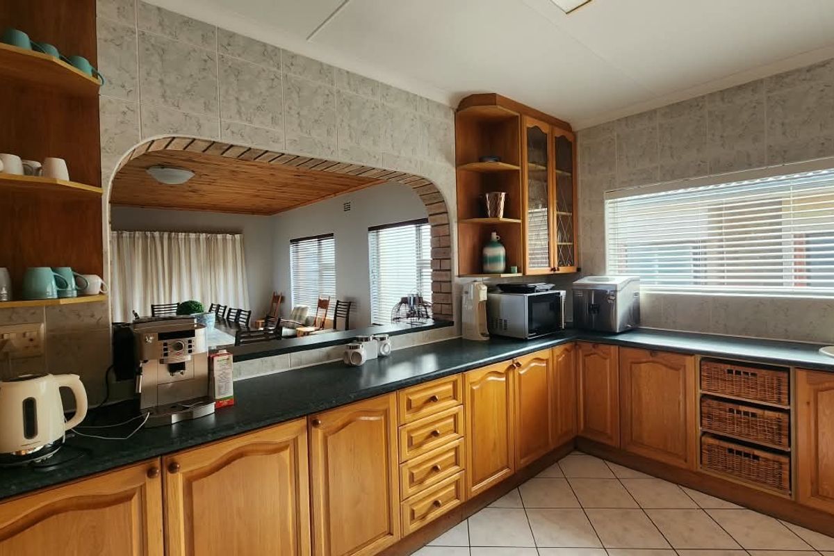 A functional kitchen featuring wooden cabinetry, laminate countertops, tiled backsplash, and an open-plan archway connecting to the adjacent living area.