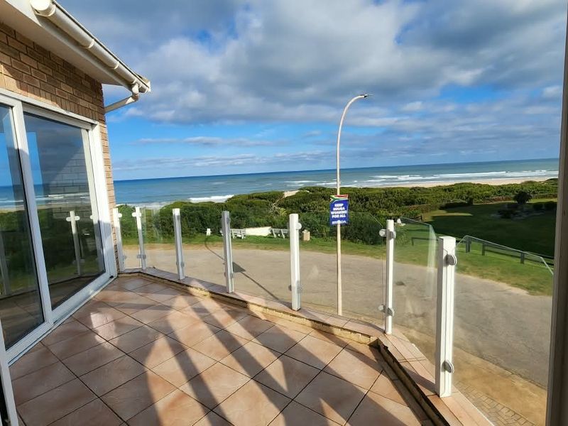 A spacious balcony featuring a modern glass balustrade and tiled flooring, offering expansive views of the coastline and surrounding landscape.