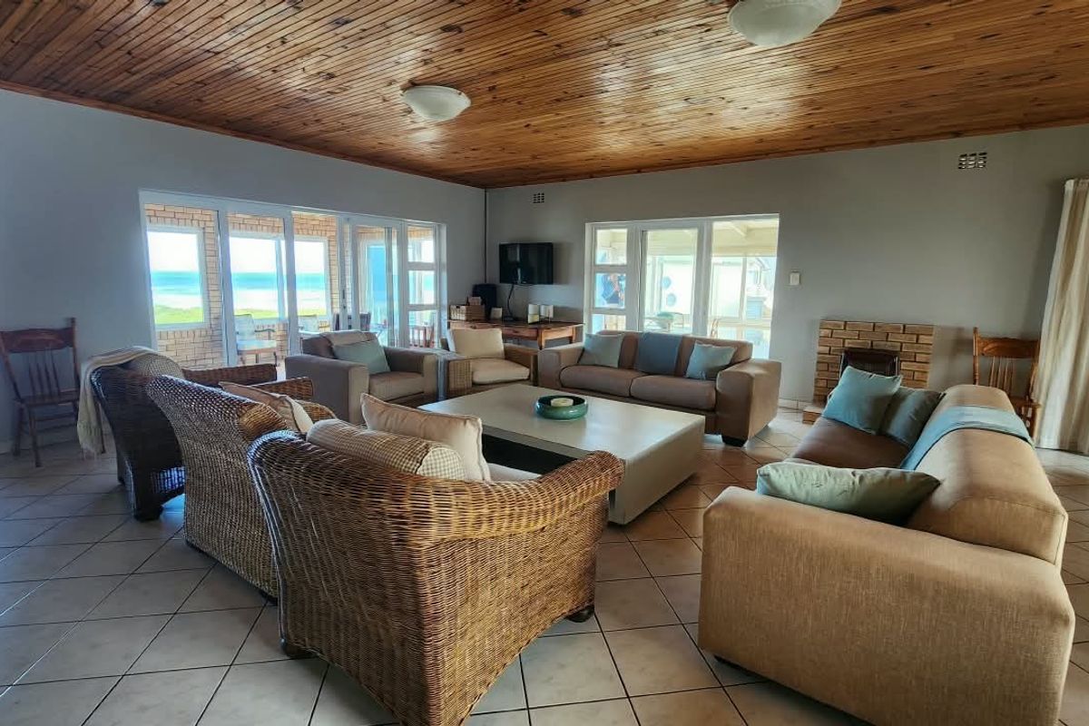 Spacious living room featuring a timber-clad ceiling, tiled flooring, and a brick fireplace, with large sliding glass doors offering views of the ocean.