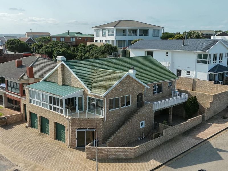 Aerial view of a multi-level brick house featuring a green tiled roof, integrated garages, and an elevated balcony in a residential neighborhood.