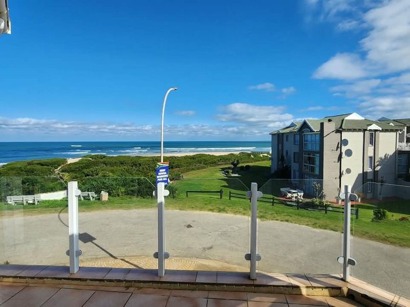 A spacious balcony featuring a modern glass balustrade and tiled flooring, offering expansive views of the coastline and surrounding landscape.