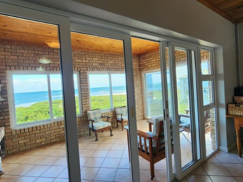 Enclosed patio featuring brick walls, timber ceiling, tiled flooring, and a built-in fireplace, offering expansive ocean views through large sliding glass doors.