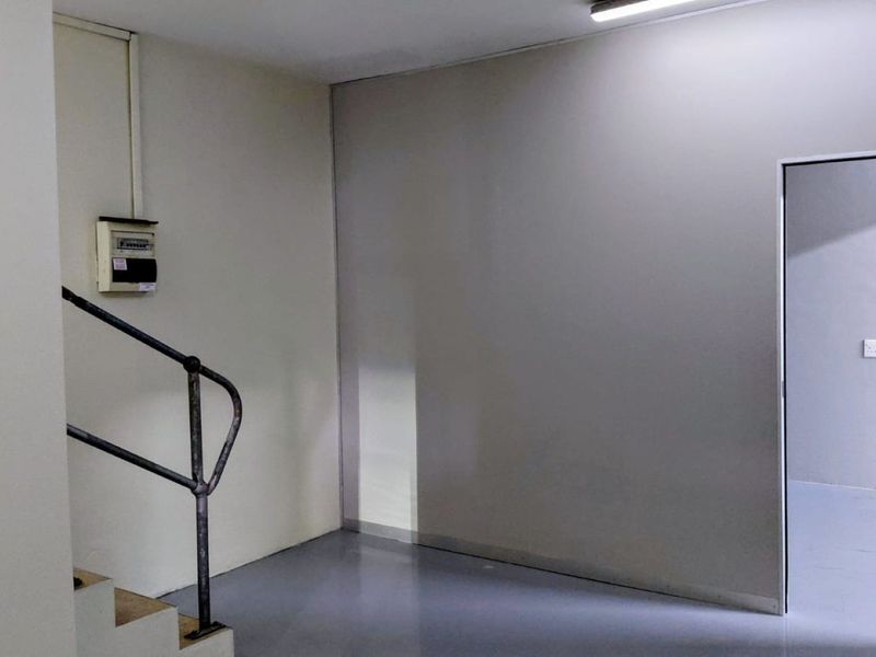 A functional industrial utility space featuring a staircase with a metal handrail, an electrical distribution board, and access to an adjacent room.