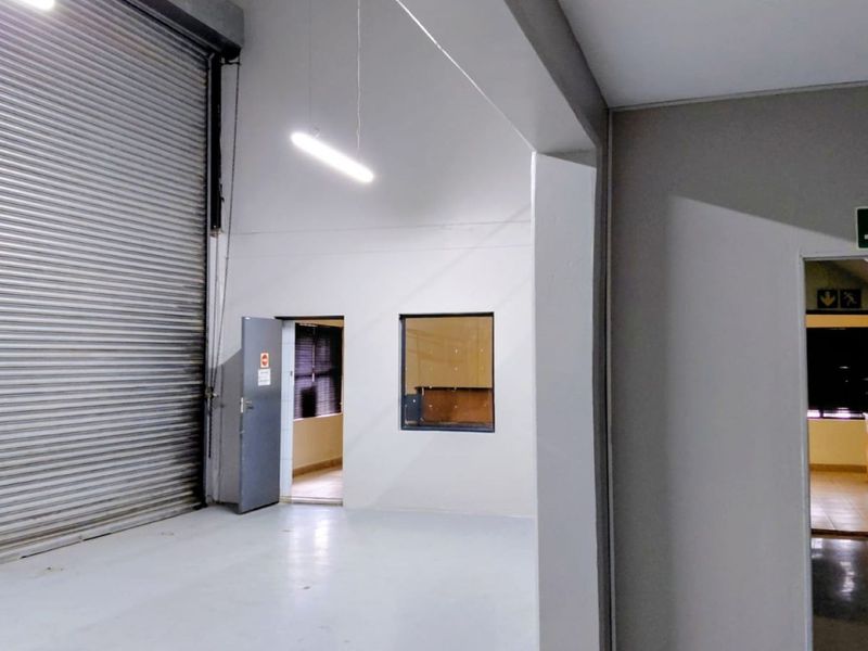 Industrial warehouse space featuring a large roller shutter door, clean painted walls, and internal access to adjacent office or utility rooms.