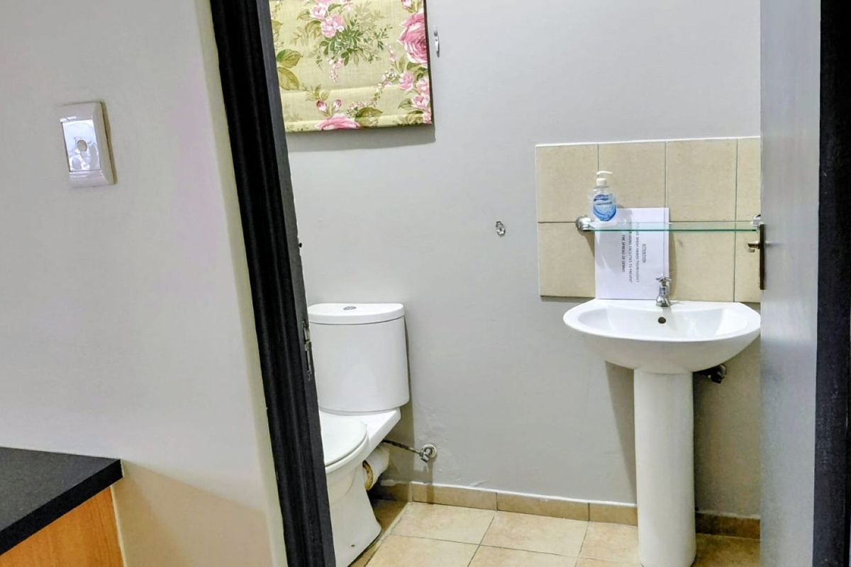 A functional bathroom featuring a pedestal basin with tiled splashback and a standard toilet, finished with tiled flooring.