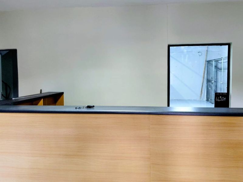 A functional reception area featuring a built-in wooden desk and an internal window looking into the adjacent industrial space.