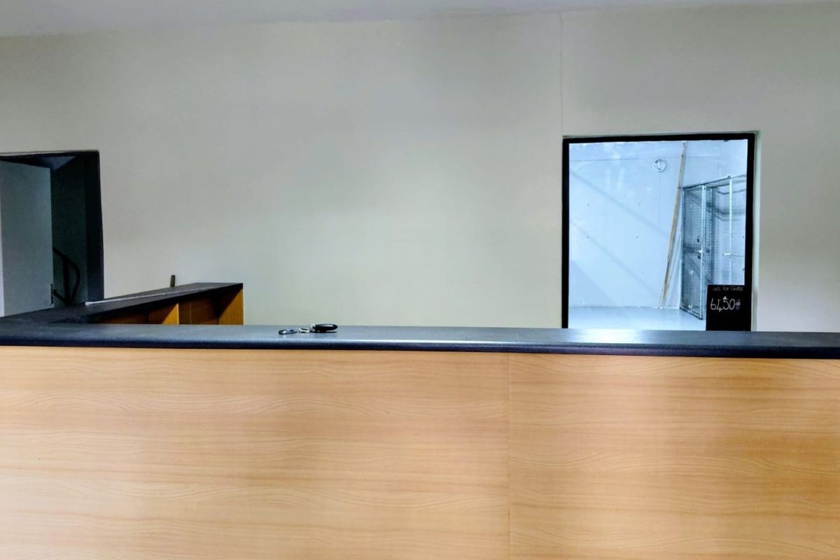 A functional reception area featuring a built-in wooden desk and an internal window looking into the adjacent industrial space.