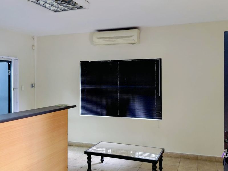 A functional office space featuring a built-in reception counter, split-system air conditioning, tiled flooring, and window blinds.