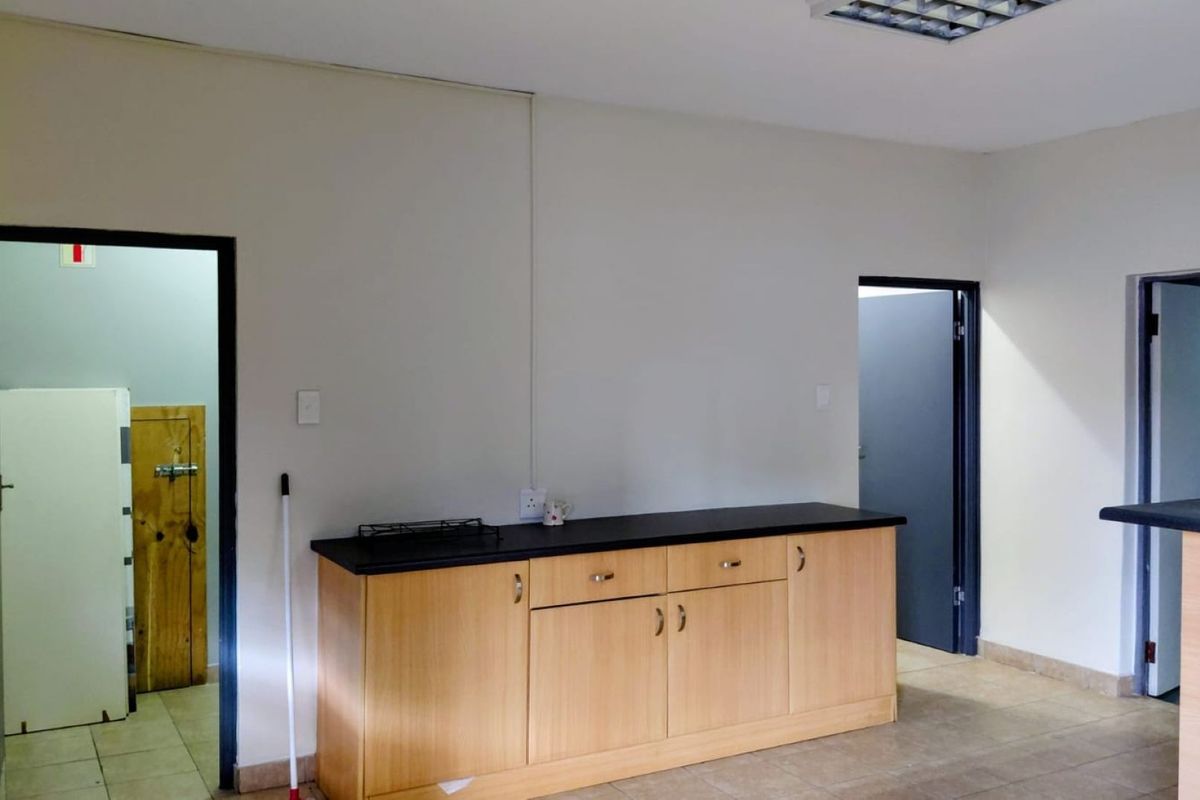 A functional kitchen area featuring light wood-finish cabinetry, a dark laminate countertop, and tiled flooring, providing a clean and practical workspace.