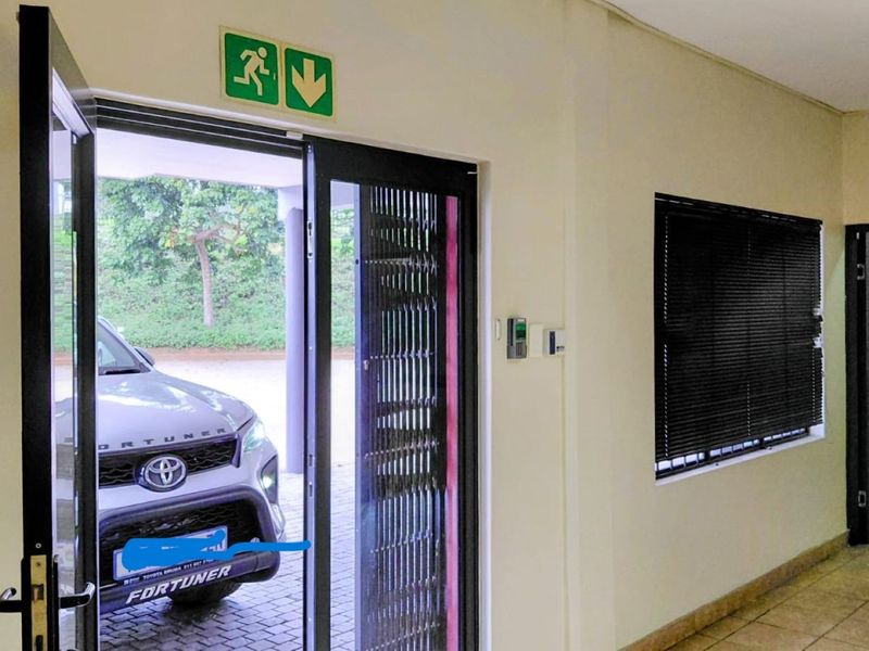 Entrance area featuring a security gate, access control system, emergency exit signage, and tiled flooring with views to the exterior.