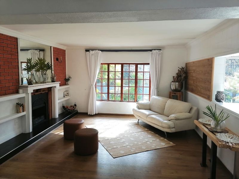 A bright living room featuring timber flooring, a classic fireplace with a brick feature wall, and large timber-framed windows allowing for natural light.