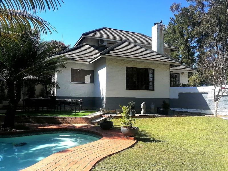Rear view of the house featuring a swimming pool, brick paved surround, and a landscaped garden area.