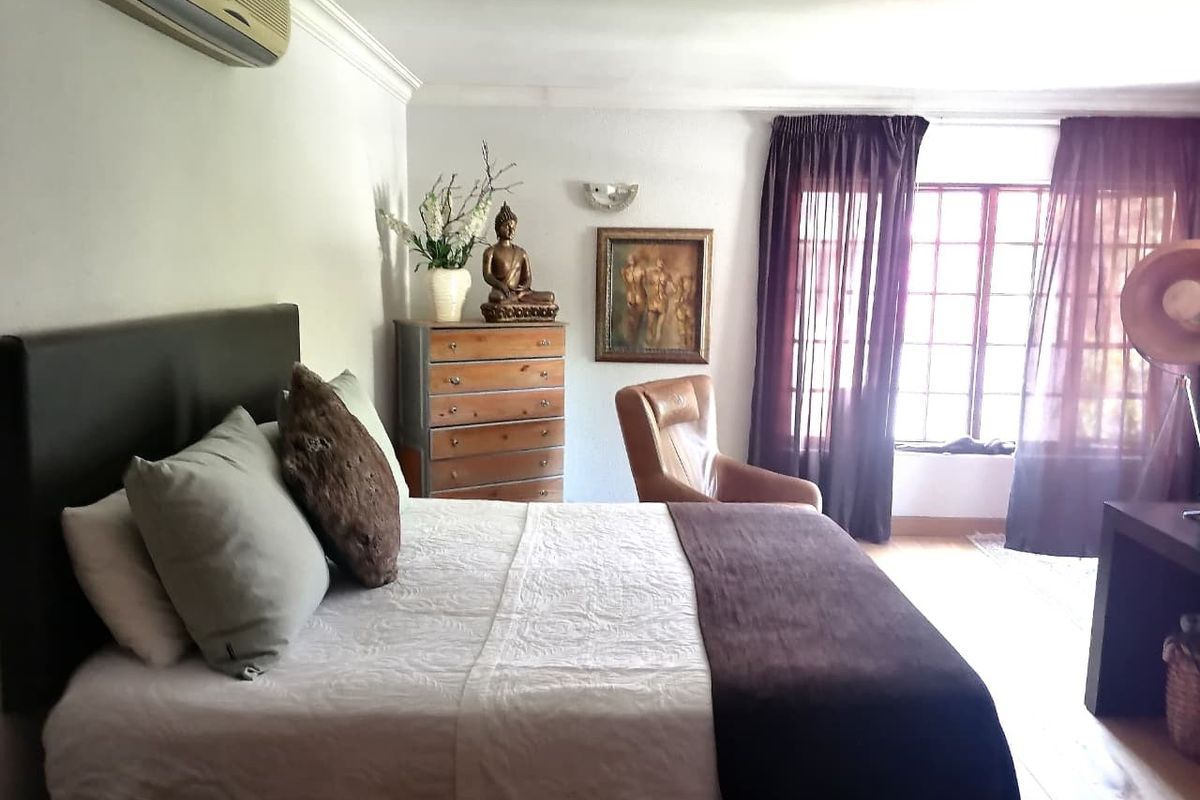 A well-lit bedroom featuring a wall-mounted air conditioning unit, timber-framed windows, and decorative coving.