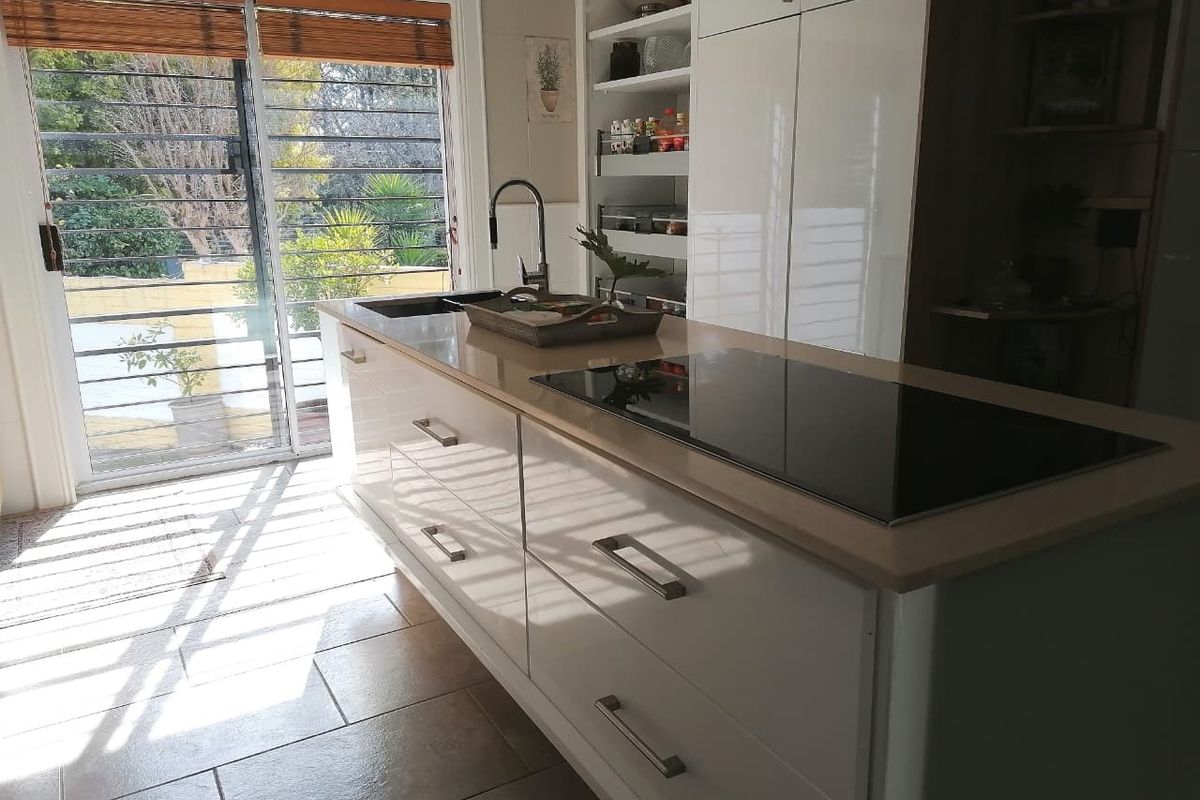Modern kitchen featuring a central island with an integrated induction hob, sleek white cabinetry, pull-out pantry storage, and direct access to the outdoor area.