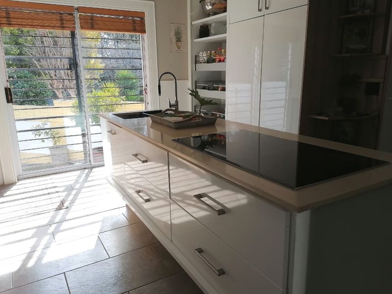 Modern kitchen featuring a central island with an integrated induction hob, sleek white cabinetry, pull-out pantry storage, and direct access to the outdoor area.