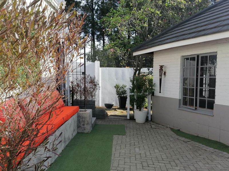 A paved outdoor patio area featuring a built-in concrete bench, brick wall construction, and a tiled roof overhang.