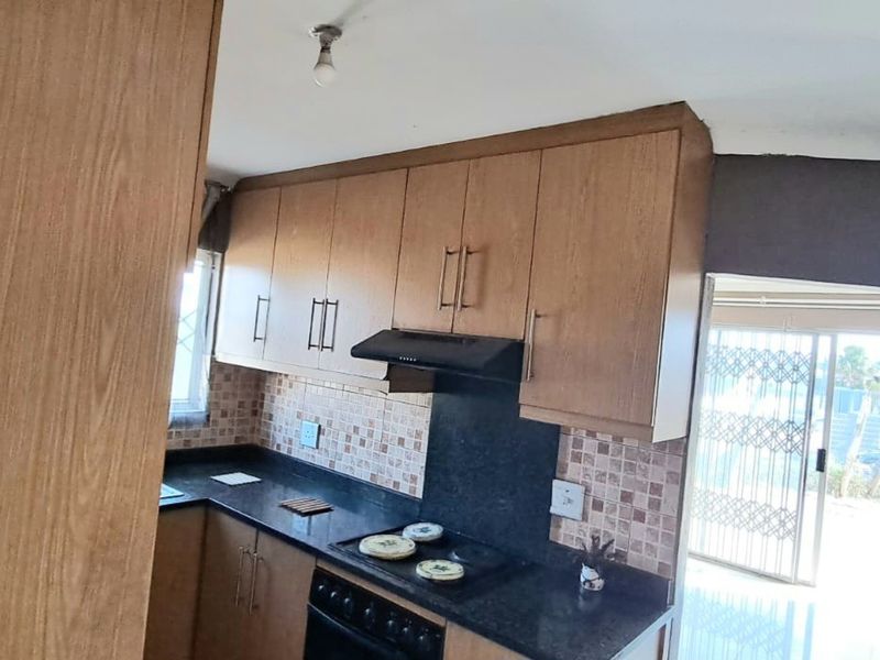 A functional kitchen featuring wood-look cabinetry, dark countertops, a tiled backsplash, and integrated cooking appliances, with direct access to an outdoor area.