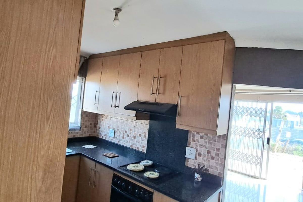 A functional kitchen featuring wood-look cabinetry, dark countertops, a tiled backsplash, and integrated cooking appliances, with direct access to an outdoor area.
