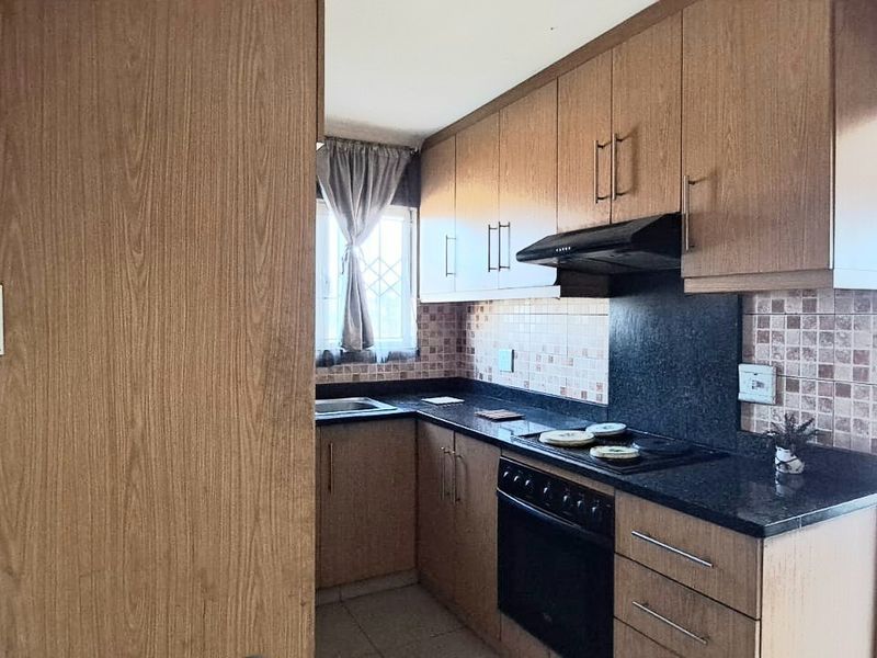 Compact kitchen featuring wood-finish cabinetry, dark laminate countertops, built-in electric stove with extractor fan, and tiled backsplash.