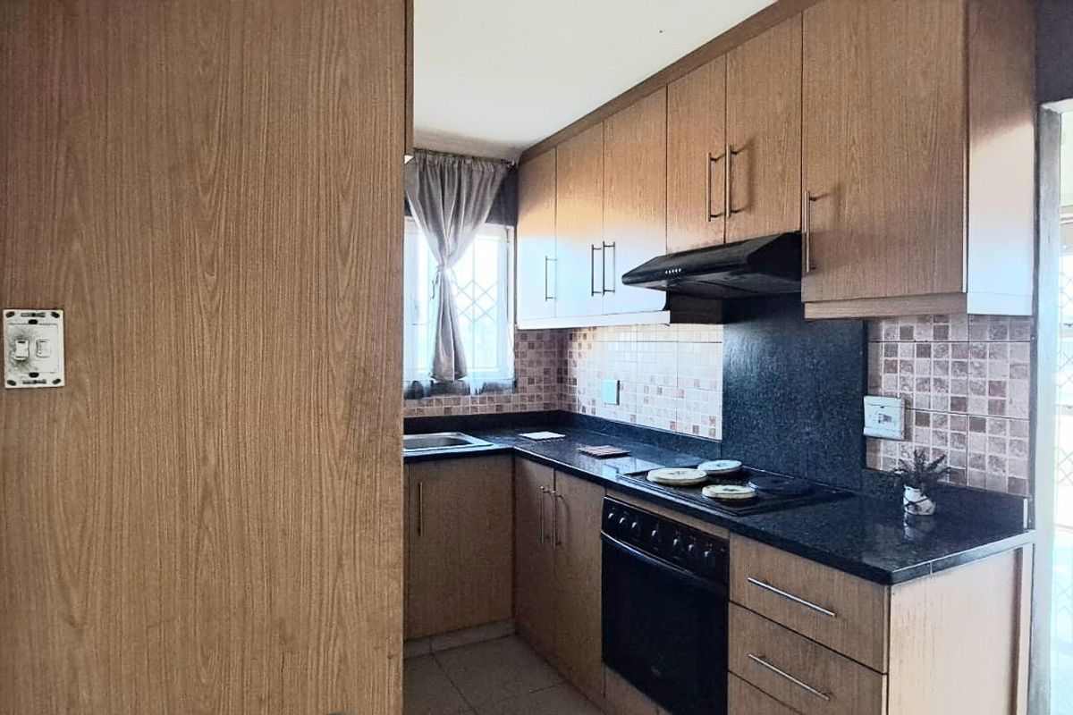 Compact kitchen featuring wood-finish cabinetry, dark laminate countertops, built-in electric stove with extractor fan, and tiled backsplash.