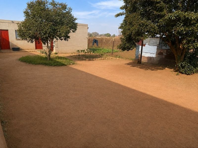 A spacious rear yard area featuring mature trees, a fenced garden section, and direct access to the main dwelling via external doors.