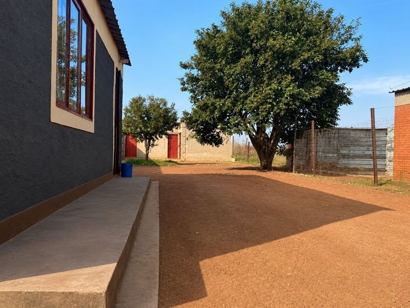 Rear exterior view of the property featuring a concrete walkway, unpaved yard area, and perimeter wire fencing.