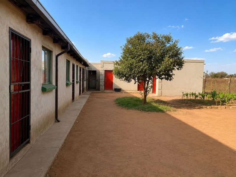 Rear exterior view of the property featuring a concrete walkway, multiple access doors with security gates, and a simple courtyard area.