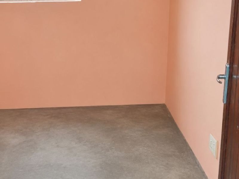 An empty bedroom featuring peach-toned walls, a concrete floor, and a window fitted with security bars.