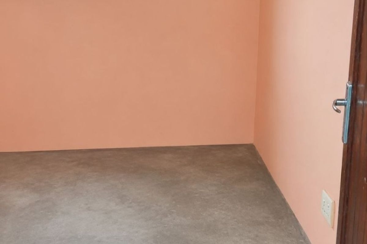 An empty bedroom featuring peach-toned walls, a concrete floor, and a window fitted with security bars.