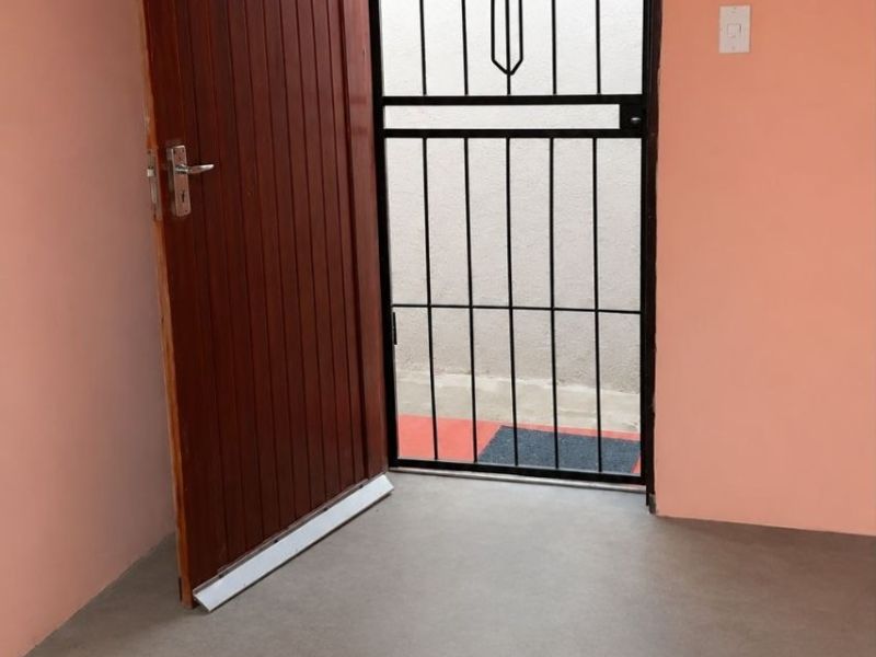 An entry area featuring a timber door, a black metal security gate, and a neutral screeded floor finish.