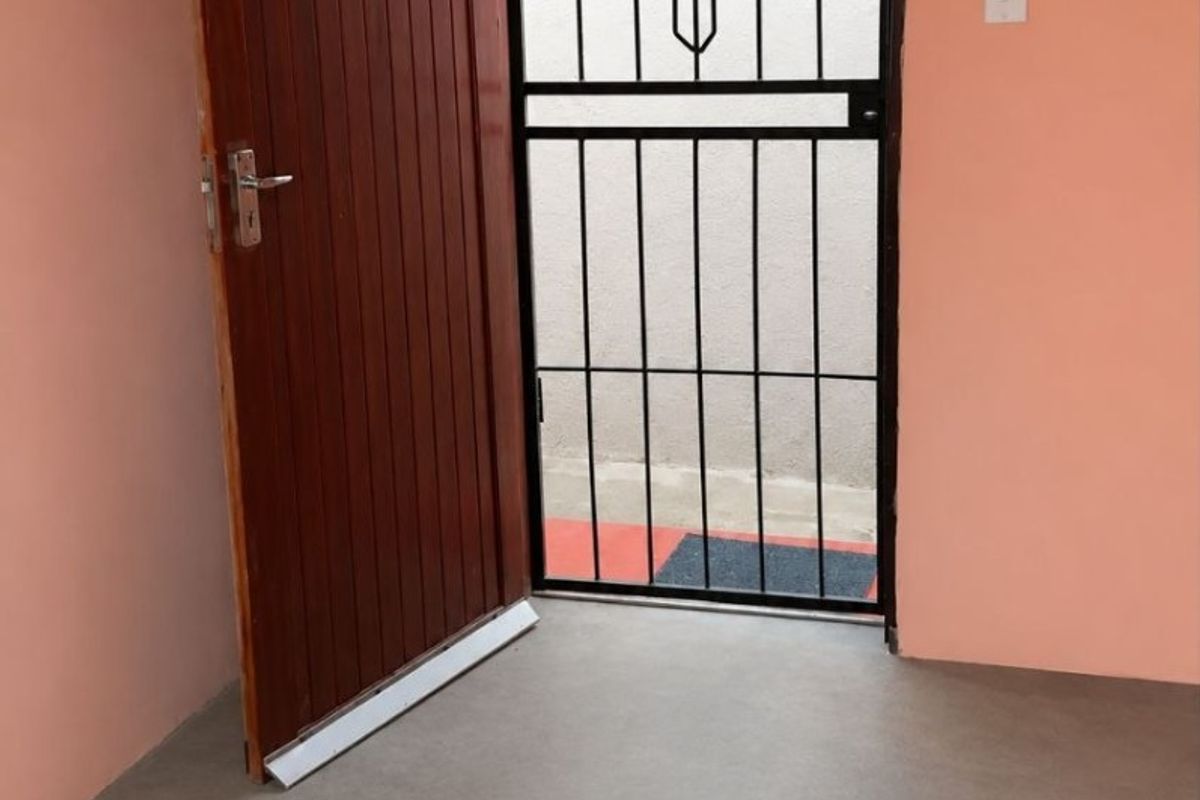 An entry area featuring a timber door, a black metal security gate, and a neutral screeded floor finish.