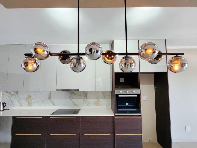 Modern kitchen featuring sleek two-tone cabinetry, marble-look splashback, built-in oven, electric hob, and a contemporary statement pendant light fixture.