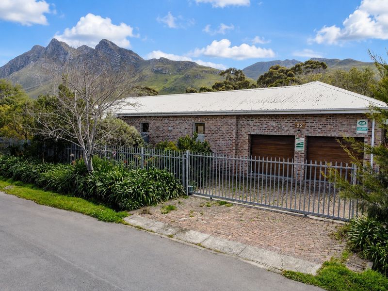 Front view of a brick-faced house featuring a double garage, metal security gate, and paved driveway, set against a scenic mountain backdrop.