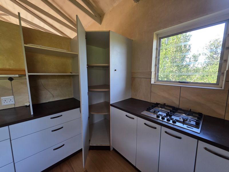 A functional kitchen area featuring built-in cabinetry, a gas hob, and a corner pantry unit, requiring cosmetic updates to modernize the space.